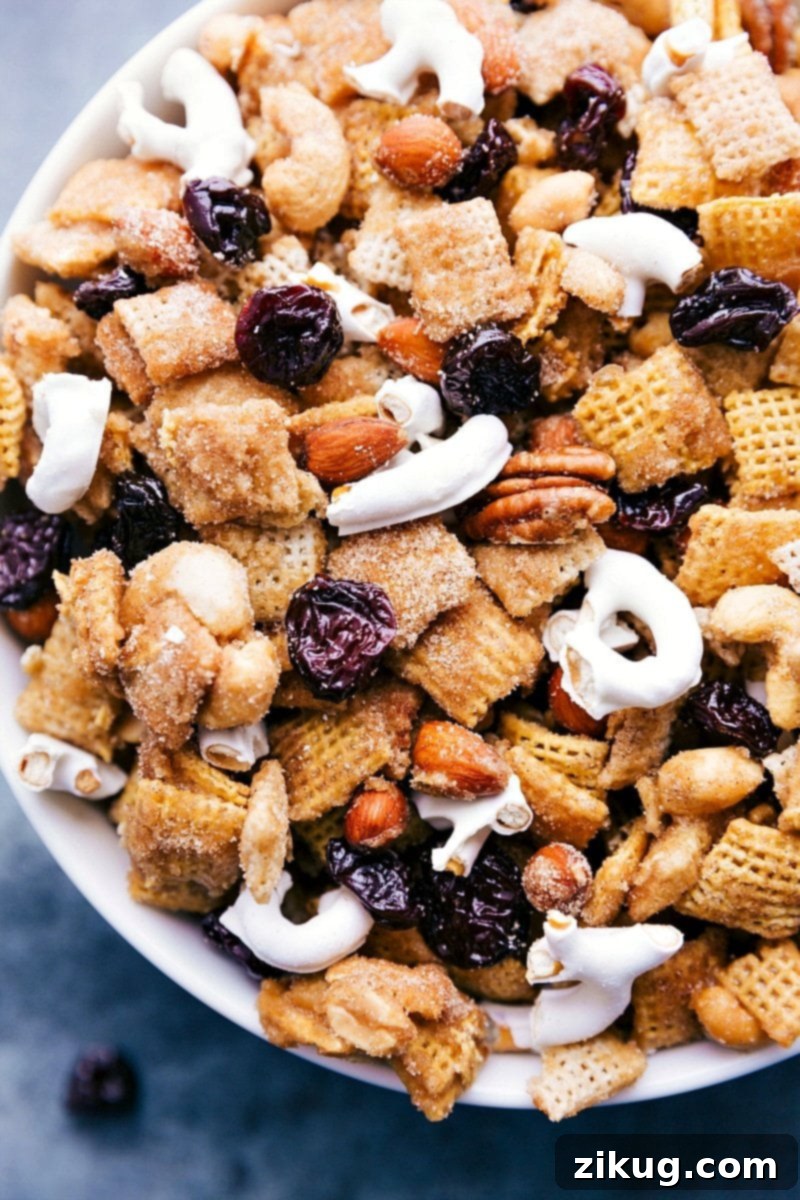 Delicious Dried Tart Cherry Snack Mix in a bowl, featuring crunchy cereal, mixed nuts, ruby red dried cherries, and white yogurt-covered pretzels, all glistening with cinnamon sugar.