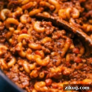 Freshly cooked goulash in a skillet with a wooden spoon, ready for serving.