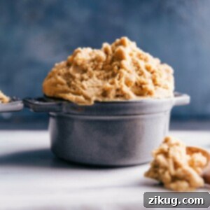 A close-up image of edible peanut butter cookie dough in a bowl, with a spoon taking a scoop, highlighting its creamy, ready-to-eat texture.