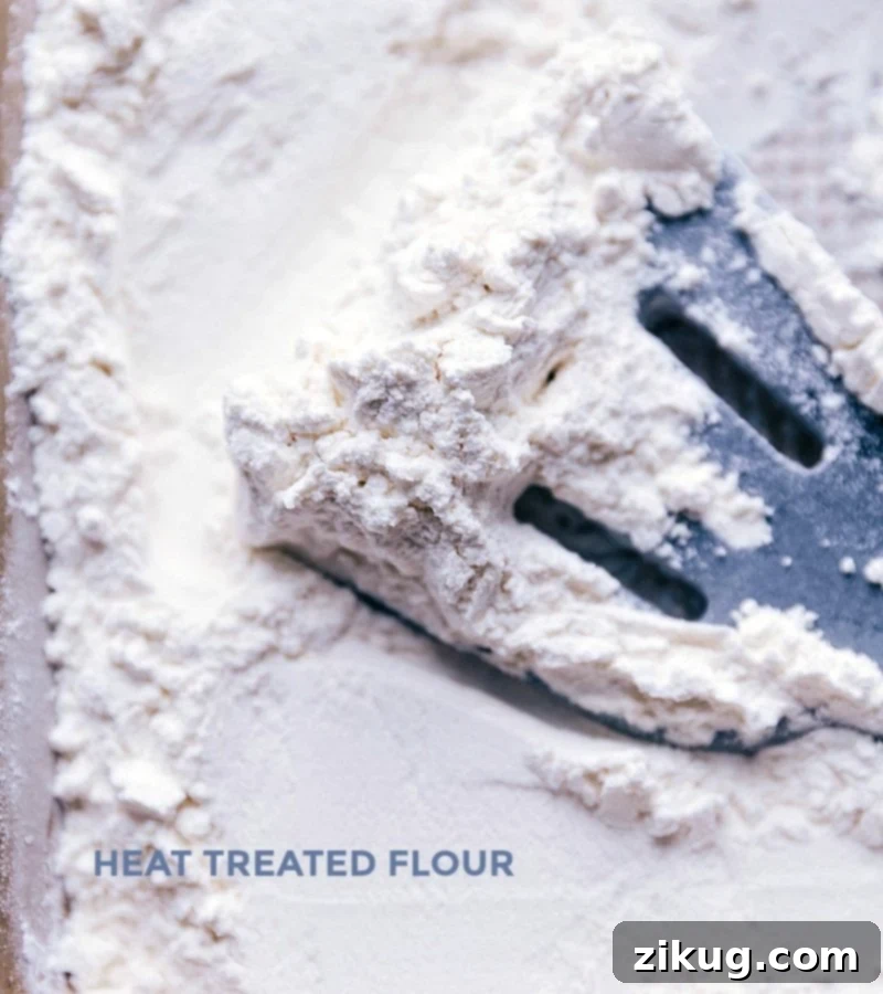 All-purpose flour spread evenly on a baking sheet, being heat-treated in an oven, an essential step for safely consuming raw dough.