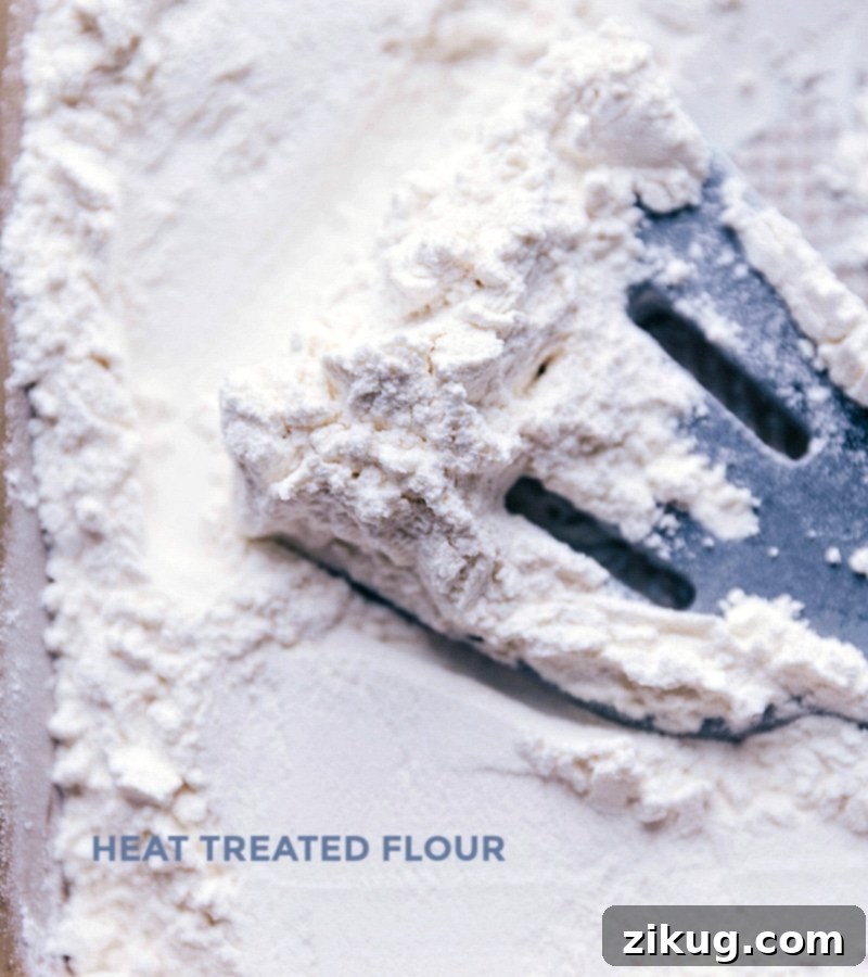 Flour spread on a baking sheet being heat-treated in an oven, a crucial step to ensure the dough is safe to consume raw.