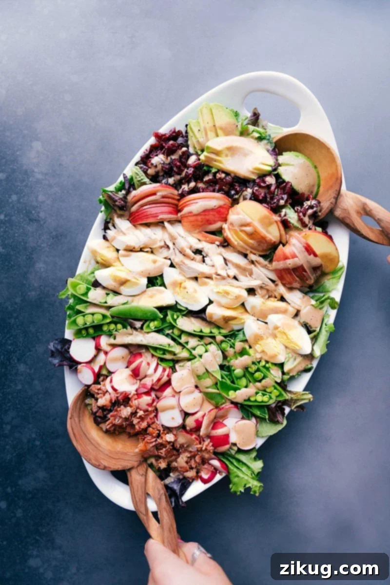 Lavish Cobb Salad Presentation with a Medley of Ingredients and Creamy Balsamic Dressing A generous serving platter heaped with a cobb salad masterpiece, boasting meats, fresh vegetables, fruit, and drizzled with creamy balsamic dressing.