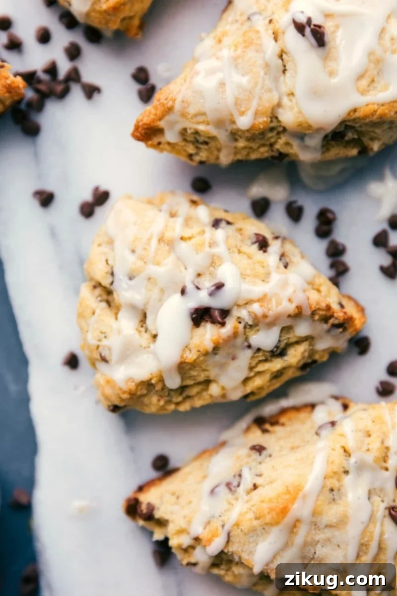 Ultimate Chocolate Chip Scones 2 Irresistible chocolate chip scones piled high, drizzled with a luscious glaze and adorned with scattered chocolate chips, inviting you to indulge in their sweet perfection.