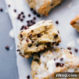 A stack of golden brown chocolate chip scones, one with a bite taken to reveal the tender, flaky interior with melted chocolate chips.