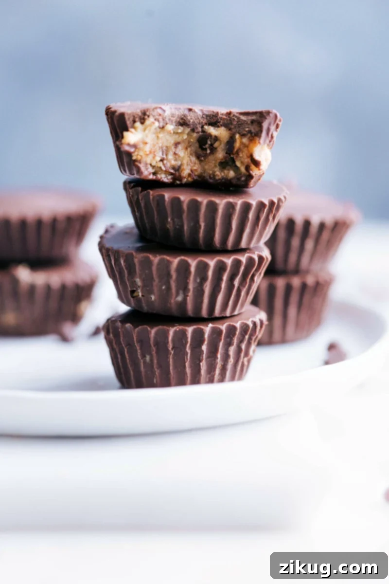 Healthy Cookie Dough Cups: Healthy food never tasted so great! Photo of several Healthy Cookie Dough Cups stacked on a plate, showcasing their dark chocolate coating and creamy cookie dough filling.