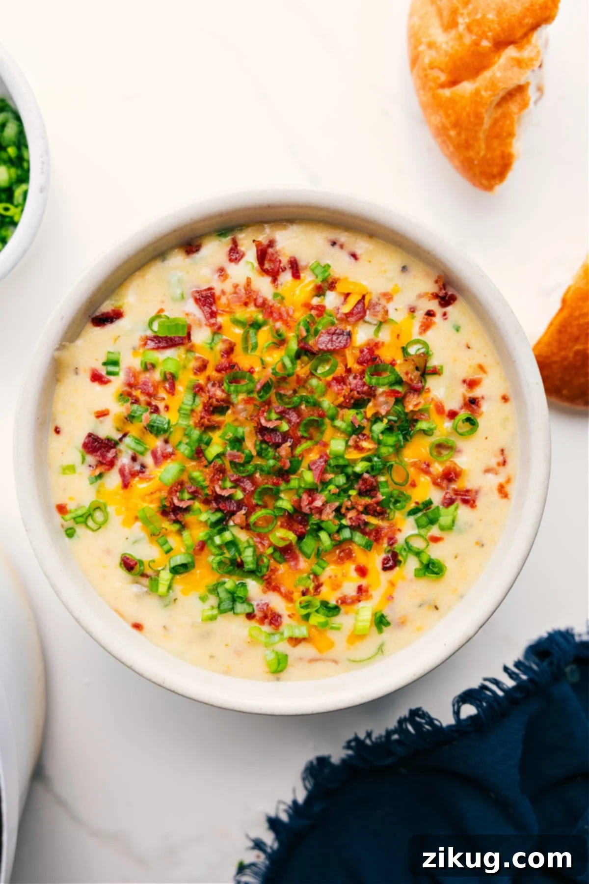 A steaming bowl of Loaded Potato Soup Recipe, garnished generously with crispy bacon bits, melted shredded cheddar cheese, and vibrant sliced green onions, ready to be enjoyed.
