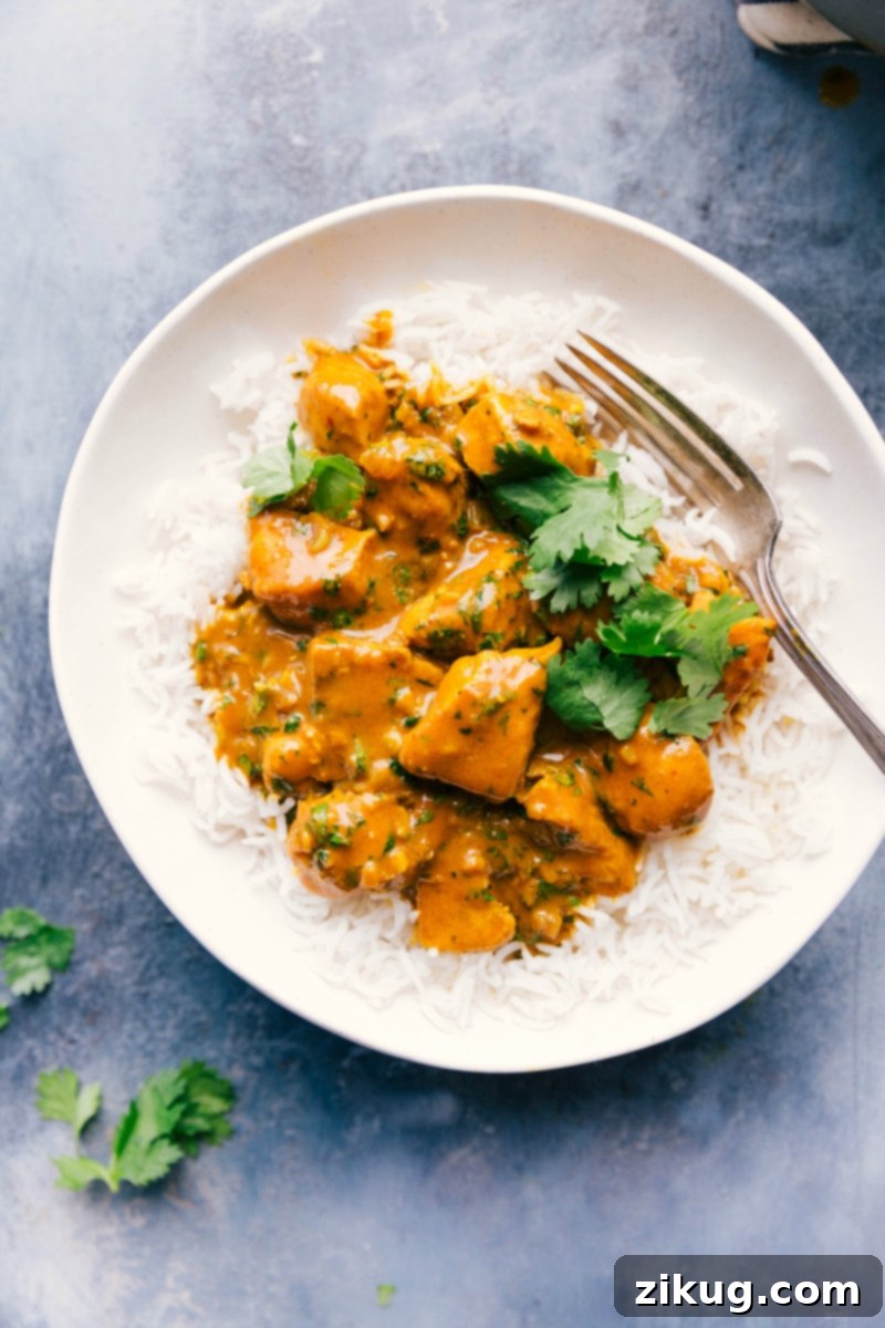 Overhead image of a generous serving of creamy Chicken Curry over basmati rice in a white bowl, with a fork resting beside it.