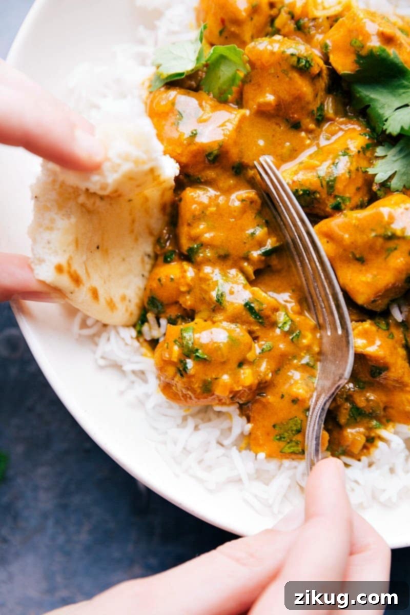 Up-close image of Chicken Curry being scooped from a bowl with a fork, showing the creamy texture and tender chicken pieces, with a piece of naan bread visible.