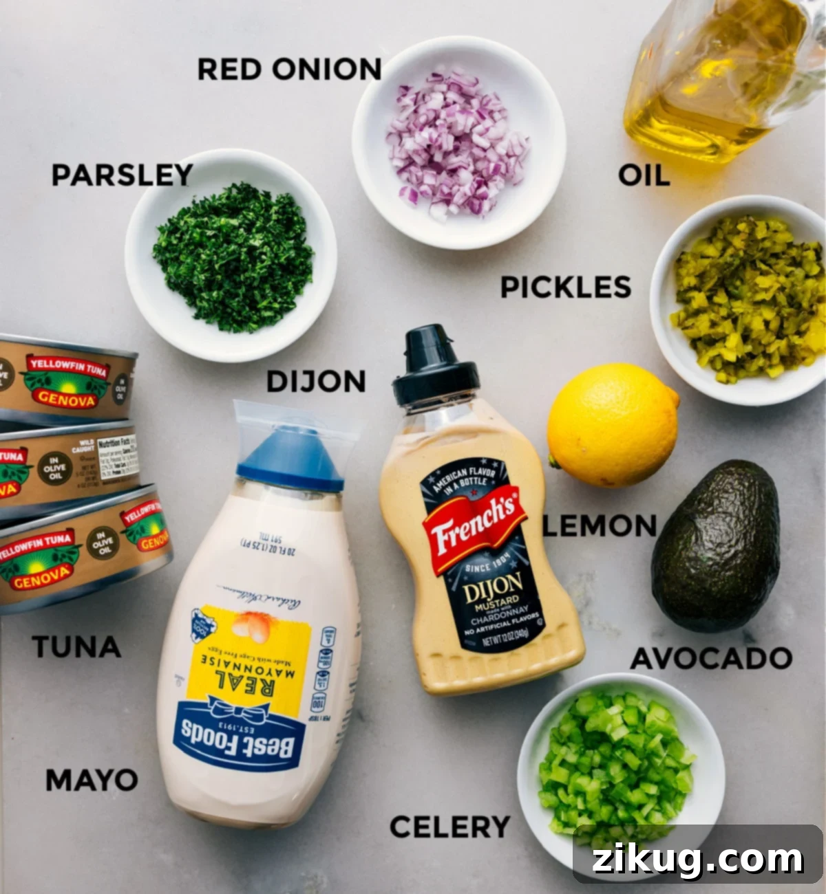 Essential Ingredients for Creamy and Flavorful Avocado Tuna Salad All the vibrant, fresh ingredients meticulously laid out on a clean cutting board: cans of olive oil-packed tuna, finely diced fresh parsley, crisp red onion, sweet and tangy bread and butter pickles, a bottle of olive oil, a halved fresh lemon, a perfectly ripe avocado, a dollop of Dijon mustard, creamy mayonnaise, and crunchy celery. Each component is prepped and ready for quick assembly into a delicious and healthy avocado tuna salad.