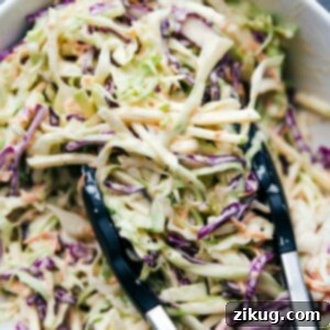 Creamy Cabbage Crunch 2 A scoop of delicious coleslaw being served with tongs, perfect to accompany BBQ Chicken Sandwiches and add a complementary flavor.