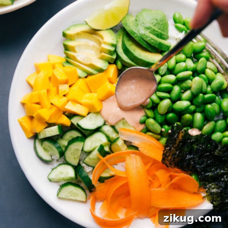 Drizzling the spicy sauce onto a fully assembled vegetarian sushi bowl with all its colorful toppings.