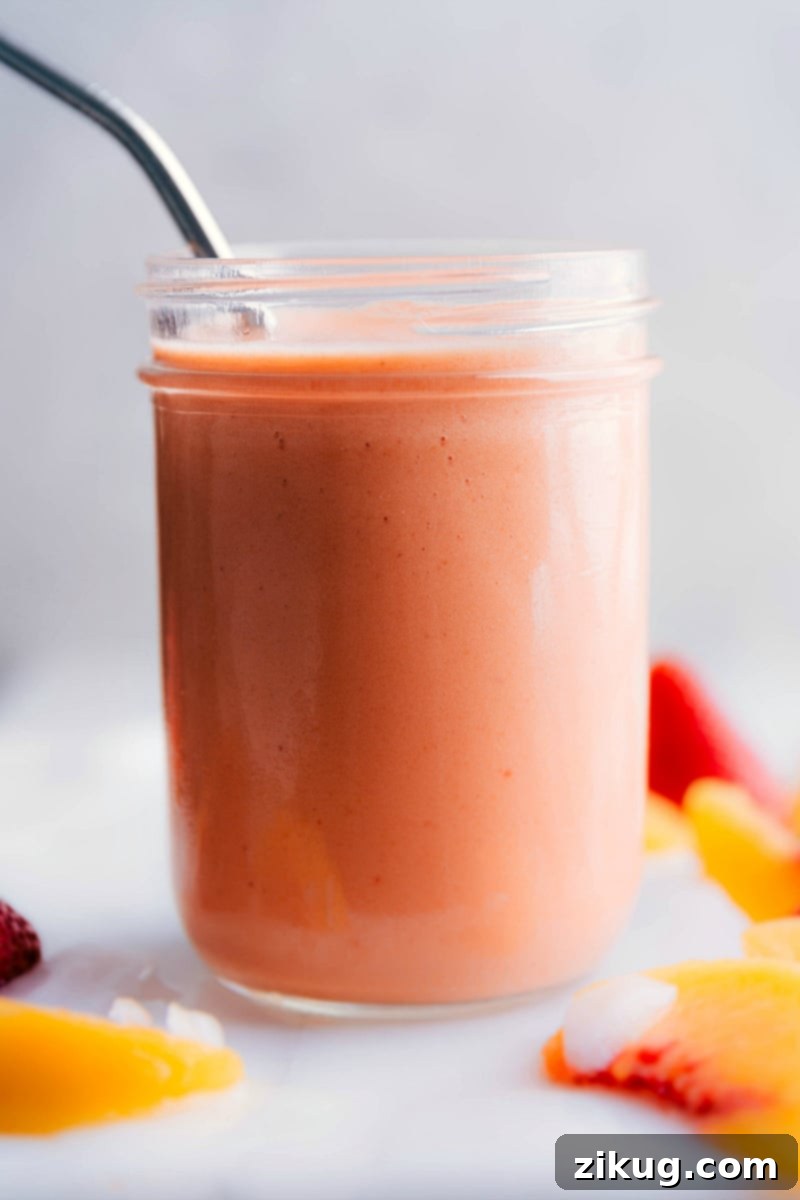 Enjoying a delicious and healthy peach smoothie fresh from the blender. A tall glass of creamy peach smoothie with a wide straw, ready to be enjoyed immediately.