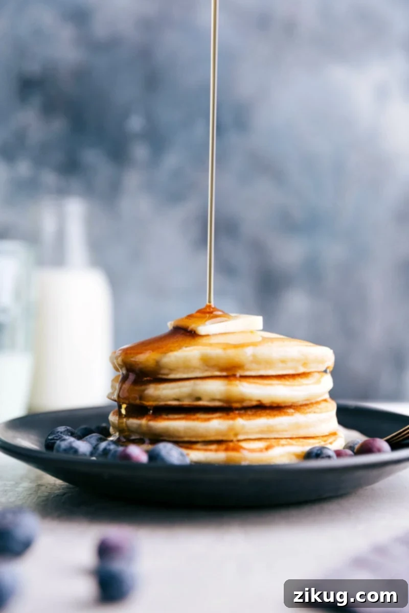 Start your day right with protein-packed Greek Yogurt Pancakes! Golden syrup being generously poured over a towering stack of fluffy Greek Yogurt Pancakes, ready to be enjoyed.