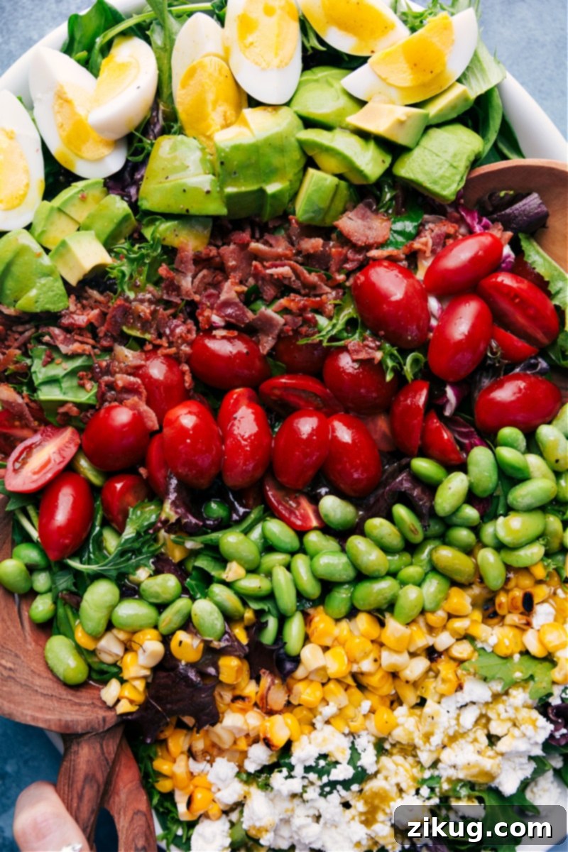 This is our favorite Cobb Salad complete with hard-boiled eggs, creamy avocado, crisp center-cut bacon, juicy cherry tomatoes, buttery edamame, sweet corn, and rich goat (or feta) cheese. It doesn't get better than this! Recipe via ChelseasMessyApron #dinner #side #best #healthy #whole #clean #cleaneating #keto #cobbsalad #herbed #vinaigrette Overhead view of Cobb Salad, showcasing its organized layers of fresh ingredients.