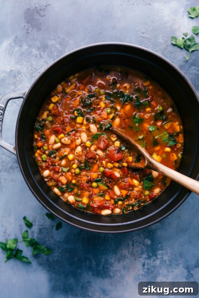 A large pot of steaming, hearty minestrone soup, brimming with vegetables and quinoa, with a wooden spoon inserted, ready to be served.