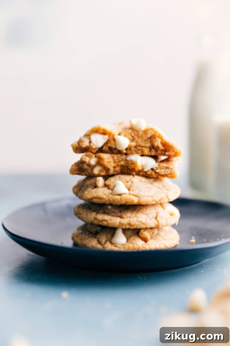 These Graham Cracker Cookies are buttery, sweet, soft, chewy, and studded with white chocolate chips and crushed graham crackers. Recipe via ChelseasMessyApron #dessert #best #quick #easy #simple #yummy #treat #chocolatechips #whitechocolate #grahamcracker #cookies A stack of golden-brown Graham Cracker Cookies, each featuring visible white chocolate chips and graham cracker pieces, presented on a rustic surface.