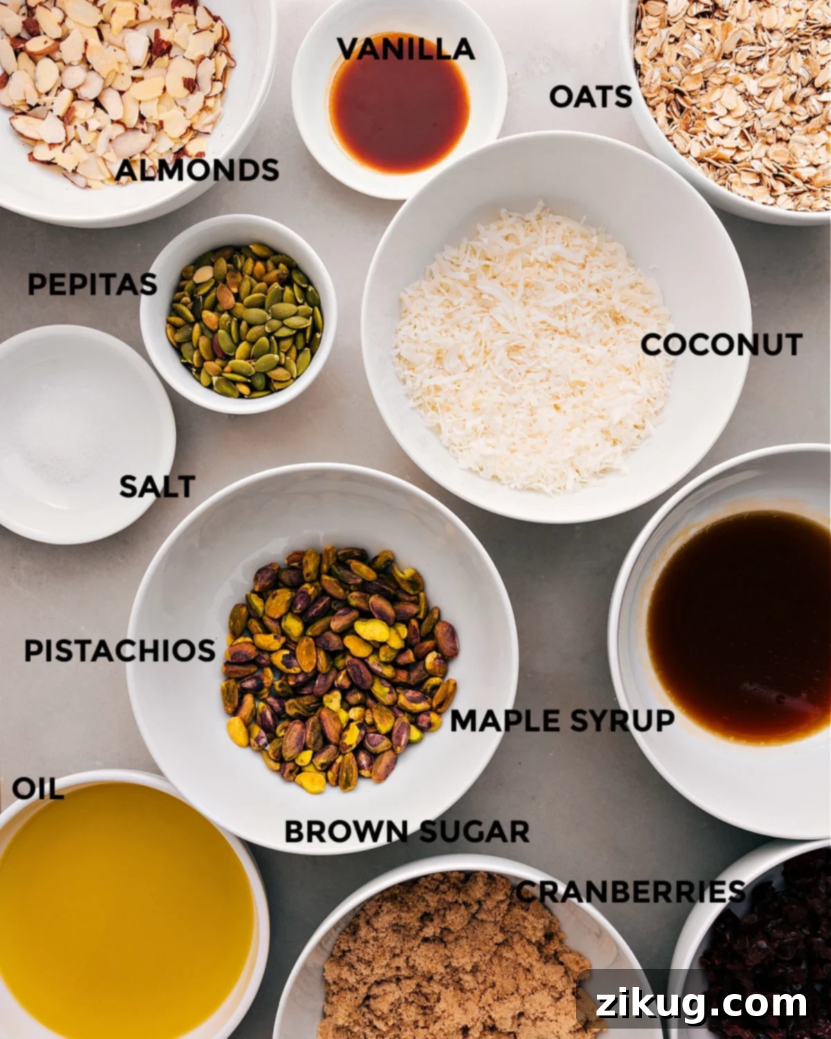 Ingredients In Homeamde Granola All the essential ingredients for making delicious homemade granola are neatly prepped and arranged: vibrant coconut flakes, hearty old-fashioned oats, fragrant vanilla extract, crunchy almonds, earthy pepitas, rich maple syrup, savory pistachios, a pinch of salt, sweet brown sugar, chewy dried cranberries, and golden olive oil.