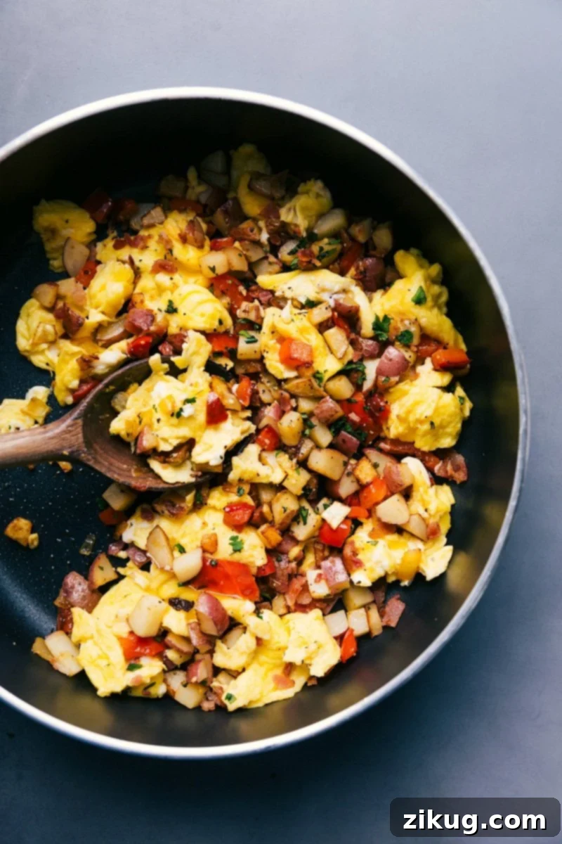 Hearty Egg Skillet Straight from the Stove, with Wooden Spoon, Prepared to Serve. The finished, savory breakfast, hot and ready for serving in a skillet.