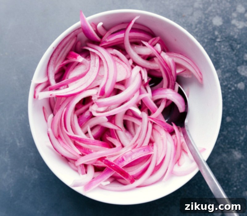 A vibrant bowl of freshly prepared pickled red onions, thinly sliced and ready to be used as a zesty topping for tacos or other dishes.