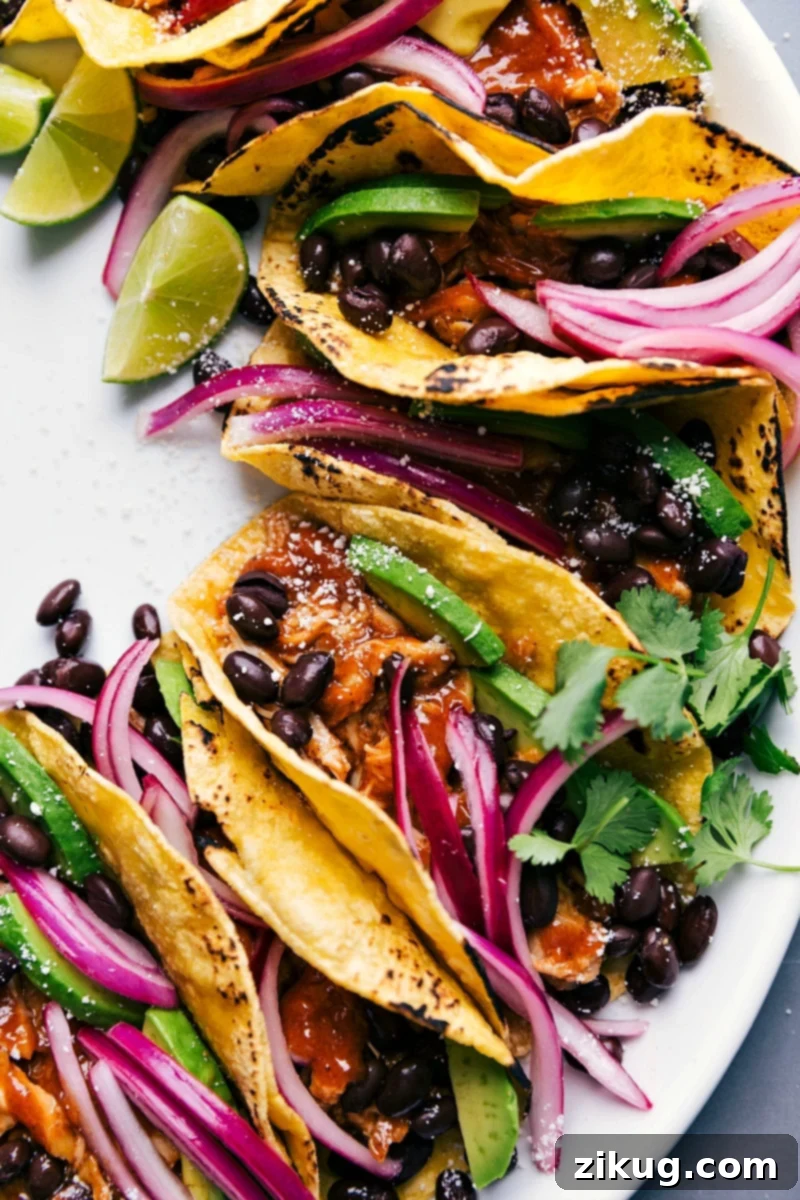 Beautifully prepared chipotle chicken tacos, garnished with fresh cilantro, a vibrant pile of pickled red onions, and other delicious toppings, ready to be enjoyed.
