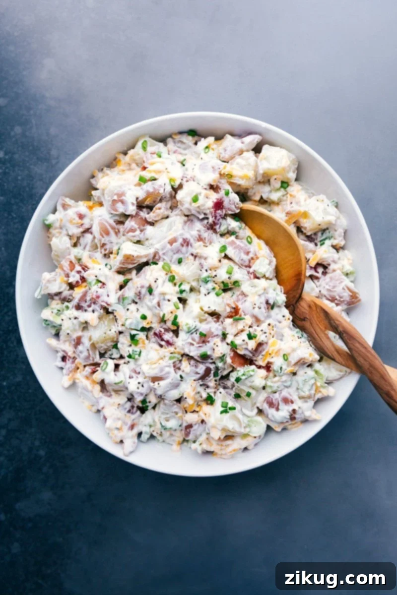 Large bowl of creamy, delicious Ranch Potato Salad, garnished with fresh green onions and crispy bacon, ready to be served at a gathering.