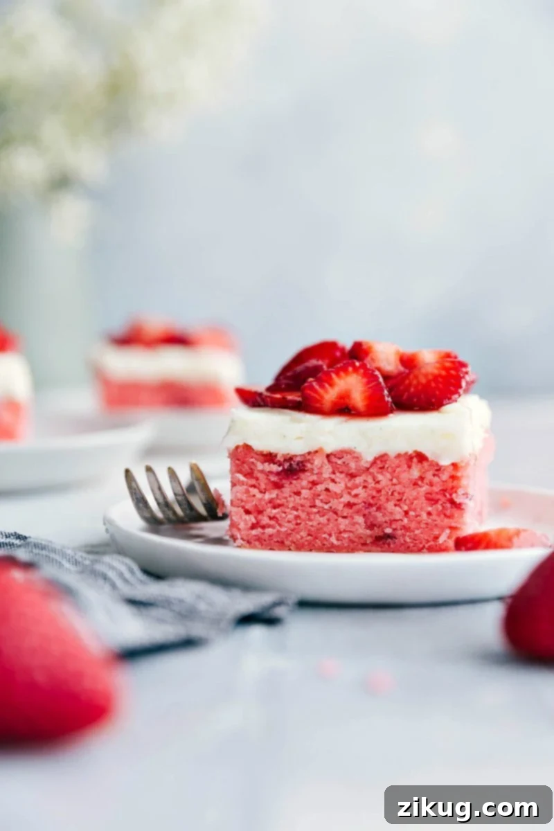 A vibrant slice of Strawberries and Cream Cake on a plate, showcasing layers of moist pink cake, thick white frosting, and fresh red strawberries.