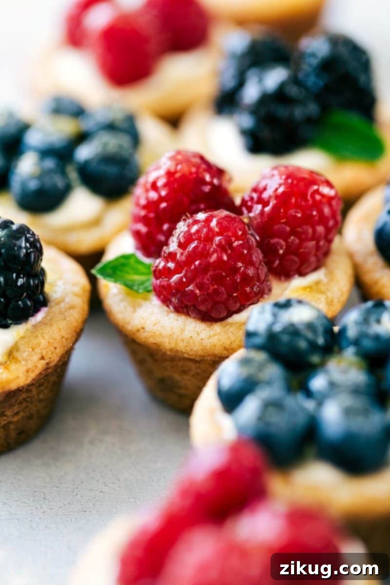 Delightful Mini Fruit Tarts Garnished with Berries and Mint Exquisite mini fruit tarts recipe adorned with fresh raspberries, blueberries, blackberries, and a sprig of mint, ready to be served.