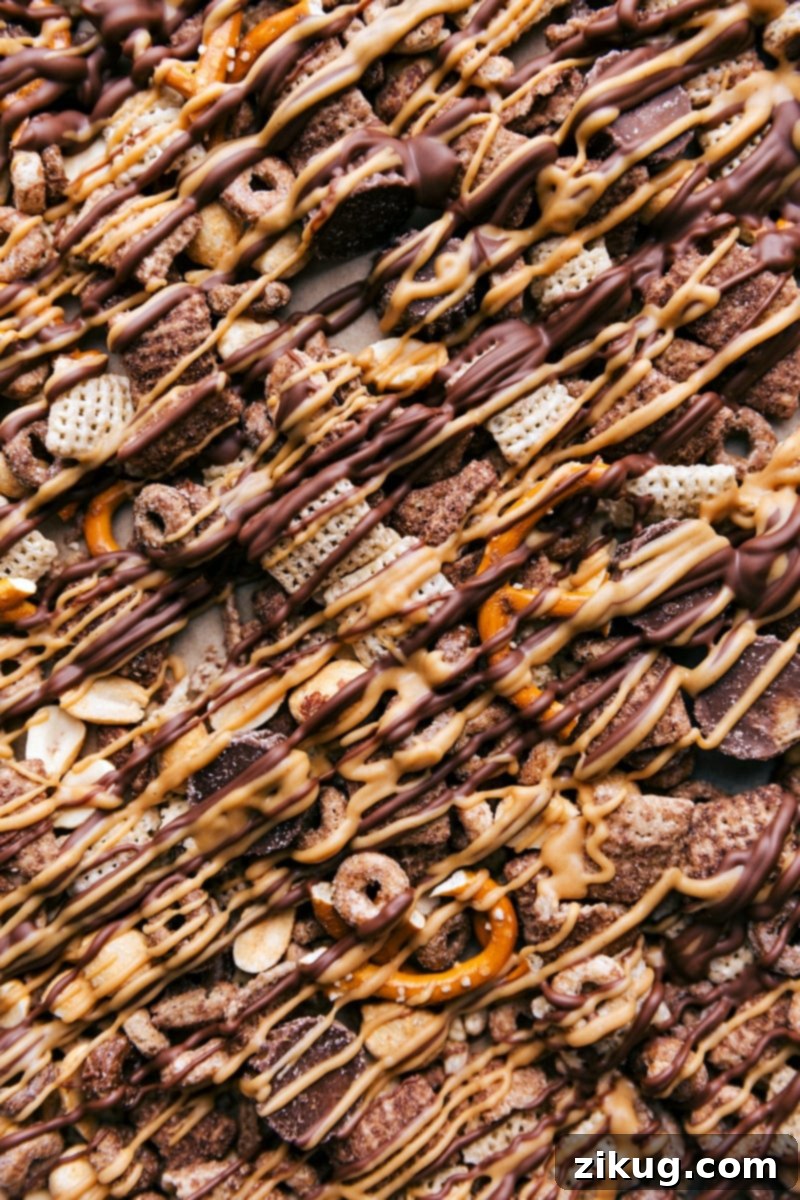 Snack Mix Masterpiece - Chocolate Peanut Butter Goodness on Display A freshly made batch of chocolate peanut butter snack mix spread on a parchment-lined baking sheet, showcasing the beautiful drizzles and mix of ingredients, ready to be chilled.