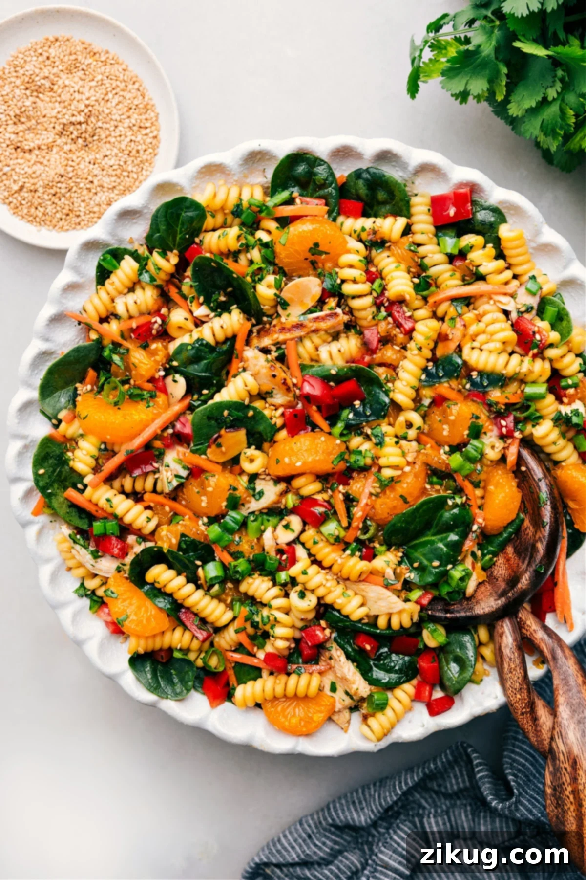 A large bowl filled with colorful Asian Pasta Salad, featuring rotini pasta, fresh vegetables, chicken, mandarin oranges, and a glistening sesame-soy dressing.