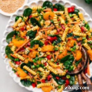 Asian Pasta Salad in a white bowl with serving utensils.