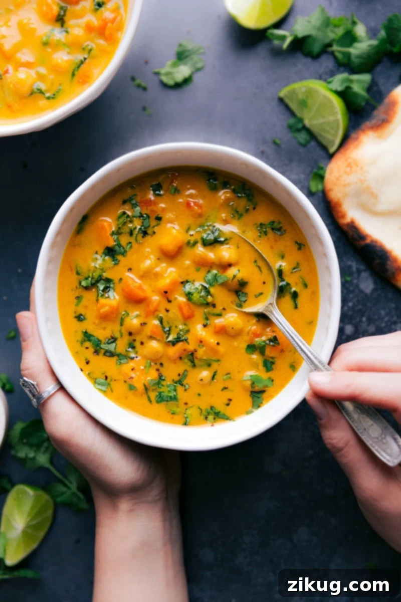 Warm Bowl of Sweet Potato Coconut Curry Soup Packed with Flavor A vibrant bowl of warm sweet potato coconut curry soup, garnished with fresh cilantro and a lime wedge, promising a burst of flavor and comfort. The creamy, rich orange soup is packed with tender sweet potato chunks and hearty chickpeas, reflecting a wholesome and satisfying meal.