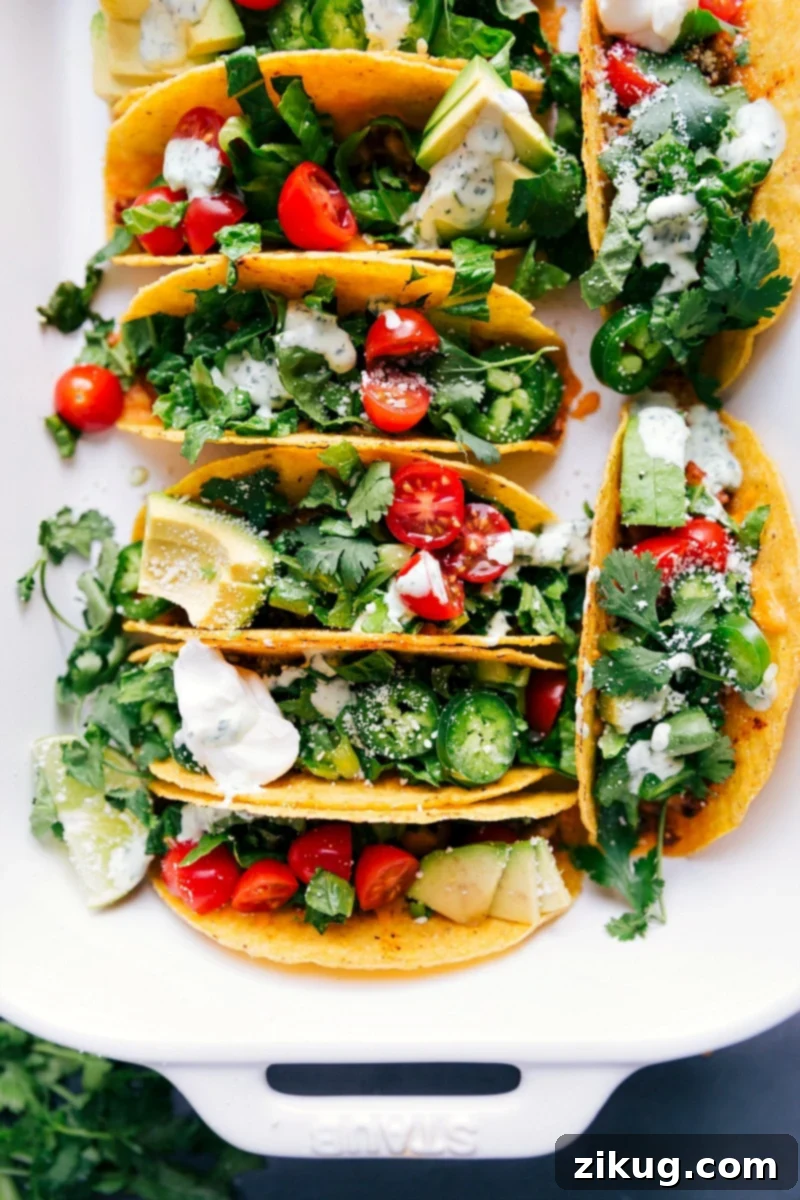 Baked chicken tacos fresh out of the oven, topped with fresh vegetables, herbs, and a delicious sauce.