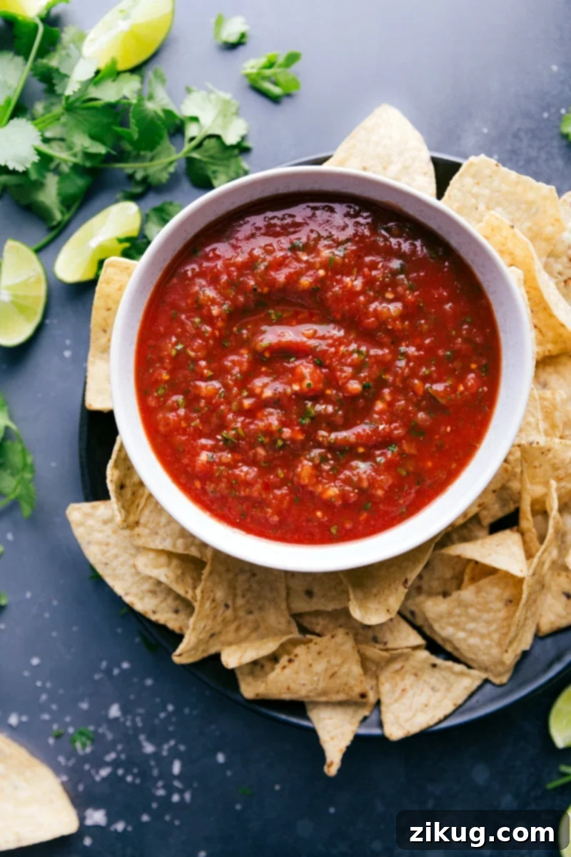 A large, inviting bowl of vibrant red homemade salsa, brimming with fresh ingredients and an enticing texture, artfully arranged alongside a generous pile of crispy, golden tortilla chips, all set for an irresistible dipping experience.