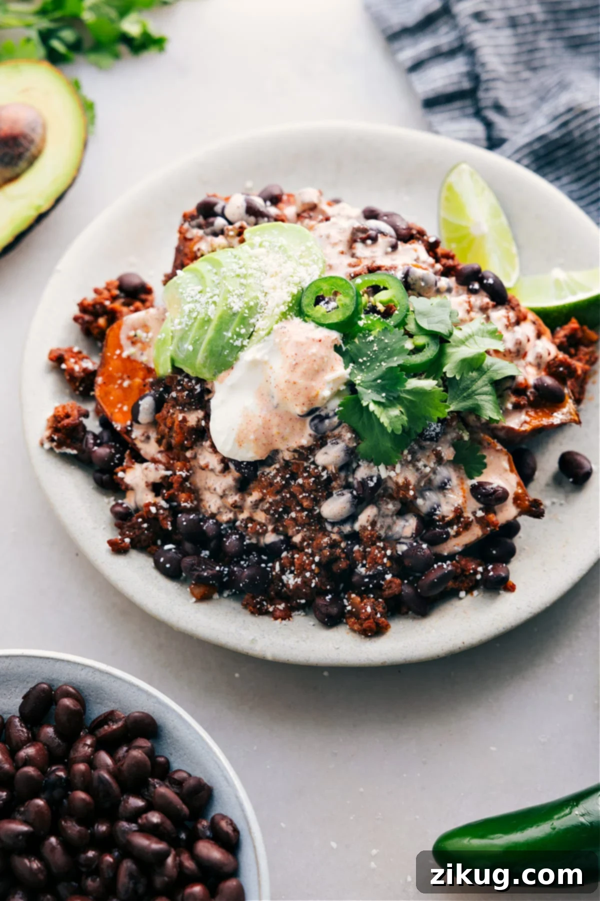 Taco Stuffed Sweet Potatoes are served on a plate and loaded with meat, avocado, sauce, jalapeño, and fresh cilantro.