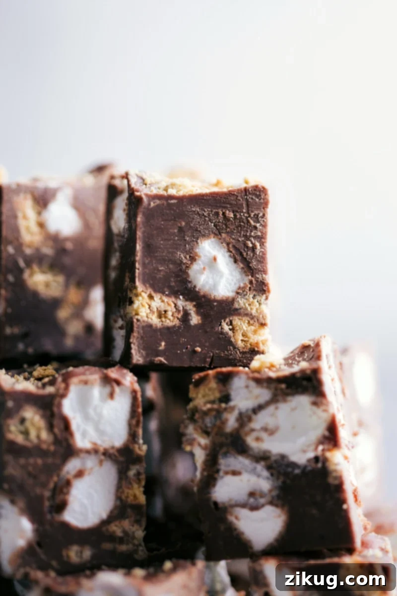 Easy Stovetop S'mores Fudge: A rich milk chocolate base loaded with crushed honey graham crackers and soft miniature marshmallows. Perfect for holidays or any sweet craving! #fudge #smoresfudge #holiday #chocolate #marshmallows #easyfudge Several pieces of rich S'mores Fudge, featuring visible graham cracker crumbs and miniature marshmallows, arranged enticingly on a serving platter.
