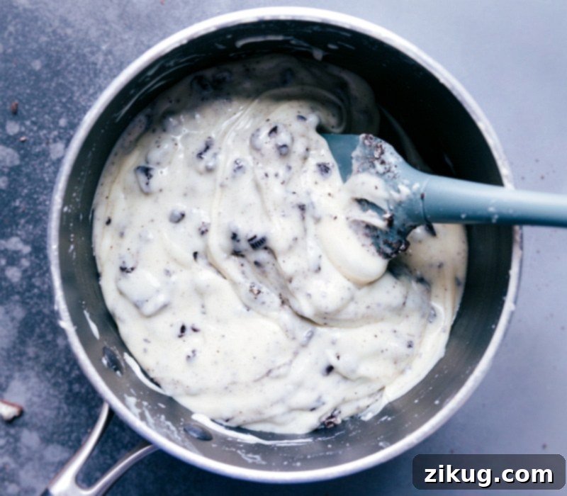 Oreo Fudge with Cookies Crushed Oreo cookies being stirred into the melted white chocolate and condensed milk mixture for the fudge.