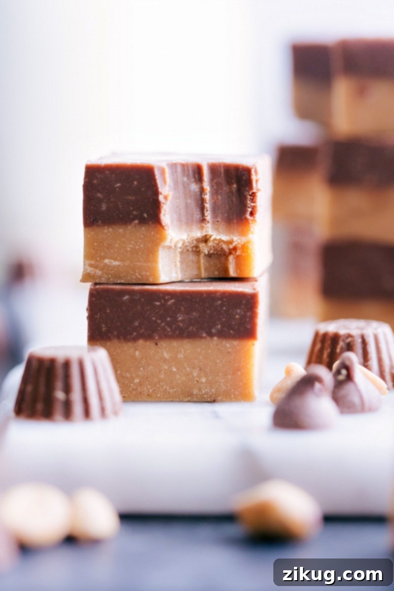 Enjoying a bite of homemade Reese's Fudge, highlighting its perfect two-layer structure. Two pieces of Reese's Fudge stacked, showing the distinct peanut butter and chocolate layers, with the top piece having a bite taken out of it.