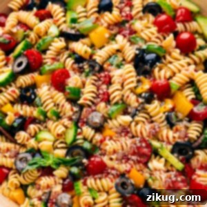 A vibrant and colorful pasta salad in a clear glass bowl, showcasing fresh ingredients like spiral pasta, cherry tomatoes, cucumbers, bell peppers, and olives, glistening with zesty Italian dressing.