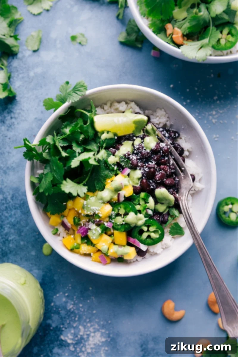 Delicious Black Bean Bowls with coconut-lime rice, saucy black beans, and mango-jalapeño topping. Overhead view of colorful Black Bean Bowls, showcasing coconut-lime rice, saucy black beans, mango-jalapeño topping, and a drizzle of cashew-cilantro sauce.