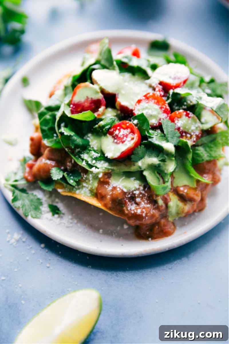 The Ultimate Bean Tostada: Crispy, Flavorful, and Ready to Savor with Avocado, Spiced Beans, Veggies, and Zesty Cilantro-Lime Sauce. A close-up, inviting image of a perfectly assembled Bean Tostada, showcasing its crispy shell, creamy avocado, rich pinto beans, fresh toppings, and a generous drizzle of cilantro-cashew sauce, ready to be enjoyed.