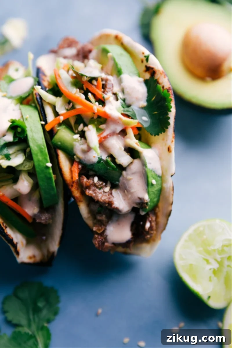 Korean Beef Tacos are a complete explosion of flavor! The tasty marinated beef is loaded into charred tortillas and topped with a quick and crunchy veggie slaw and a delicious Sriracha-lime sauce. Recipe via ChelseasMessyApron.com #tacos #Koreanbeef # slaw #charredtortilla Close-up image of Korean Beef Tacos with vibrant toppings and perfectly cooked beef.