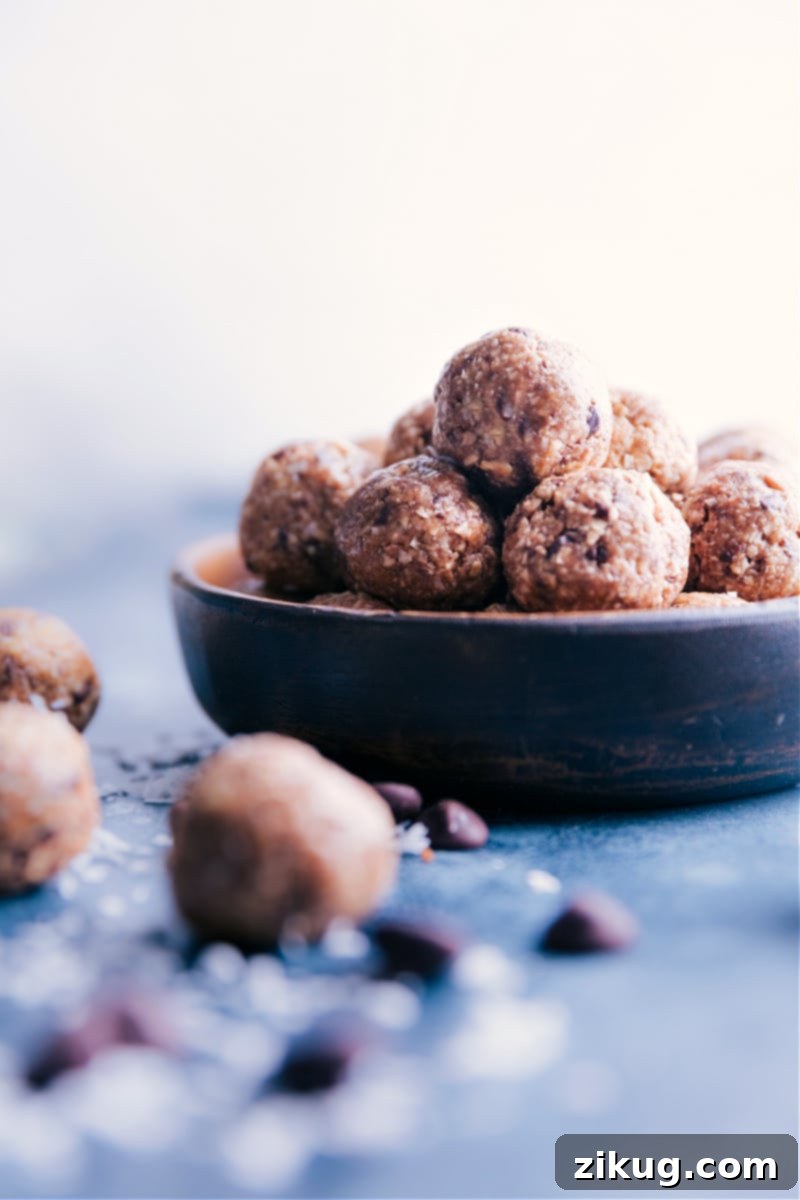 A bowl brimming with golden-brown Oatmeal Energy Balls, each with visible oats, coconut flakes, and dark chocolate chunks, resting on a rustic wooden surface.