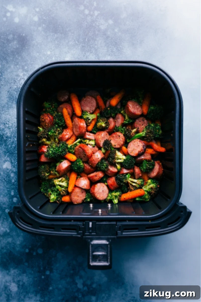 Delicious air-fried chicken sausage, carrots, and broccoli coated in honey mustard. Served with quinoa and mixed greens, this meal is nutritious, filling, and quick, making it ideal for a speedy weeknight dinner. Recipe by ChelseasMessyApron.com #airfryer #honeymustard #chicken #sausage #veggies #quinoa #healthy #dinner Overhead view of the cooked honey mustard chicken sausage and veggies in an air fryer basket, ready to be served.