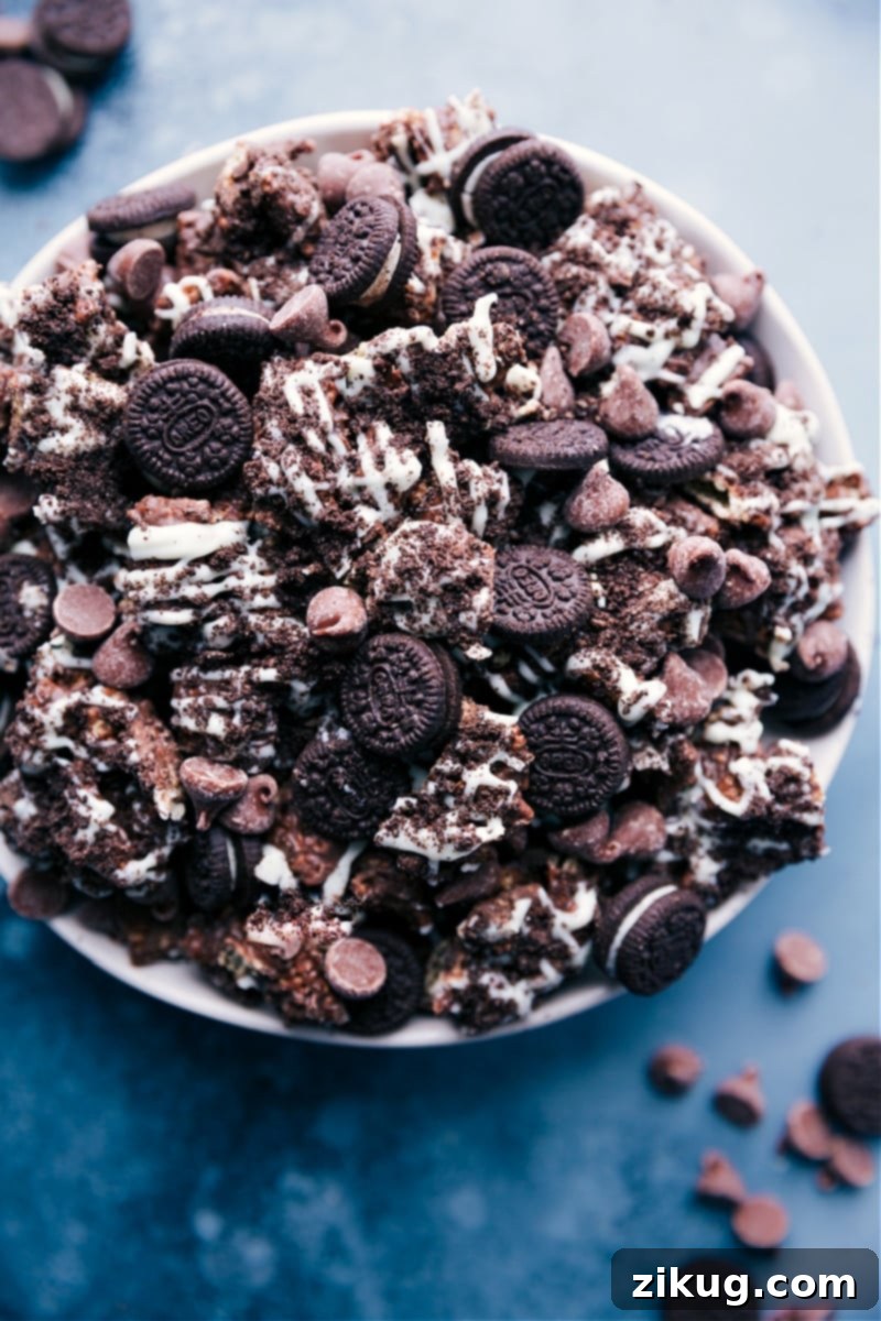 Overhead image of a large bowl filled with Cookies and Cream Muddy Buddies, featuring chocolate-covered Chex cereal, crushed Oreos, mini Oreos, and white chocolate drizzle.