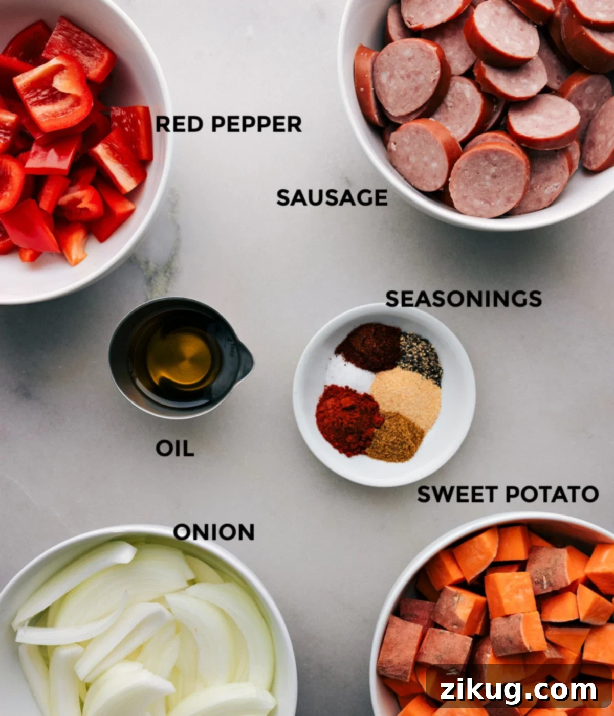 Prep Tray for Sausage and Vegetable Bake Assorted raw ingredients for cooking arranged on a tray, including sliced smoked sausage, chopped sweet potatoes, red bell pepper, yellow onion, olive oil, and a selection of seasonings, ready for preparation.
