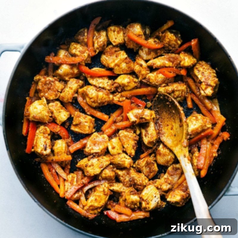 Chicken and red peppers cooking in a pan for coconut chicken curry, starting to combine with spices and flavors.