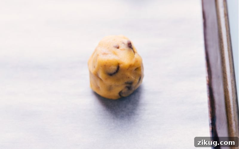 A perfectly shaped cookie dough ball, ready to be baked on a parchment-lined tray.