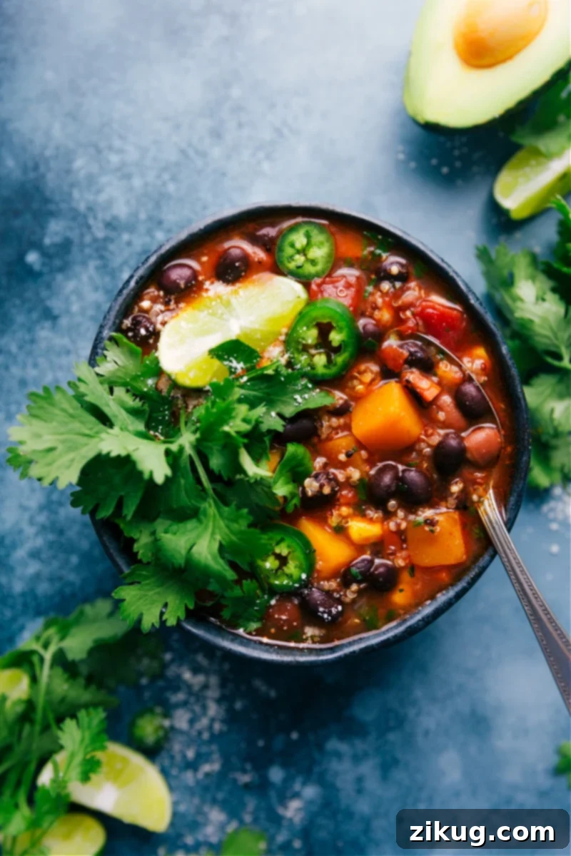 This nutritious Slow Cooker Butternut Squash Chili is bursting with flavor, packed with good-for-you ingredients like veggies, tender shredded chicken, and superfood quinoa. It's a hands-off meal thanks to the slow cooker, perfect for dinner, quick meal prep, and clean eating. Top with your favorite chili toppings and enjoy! Overhead view of a steaming bowl of Slow Cooker Butternut Squash Chili, garnished with fresh cilantro and sour cream.