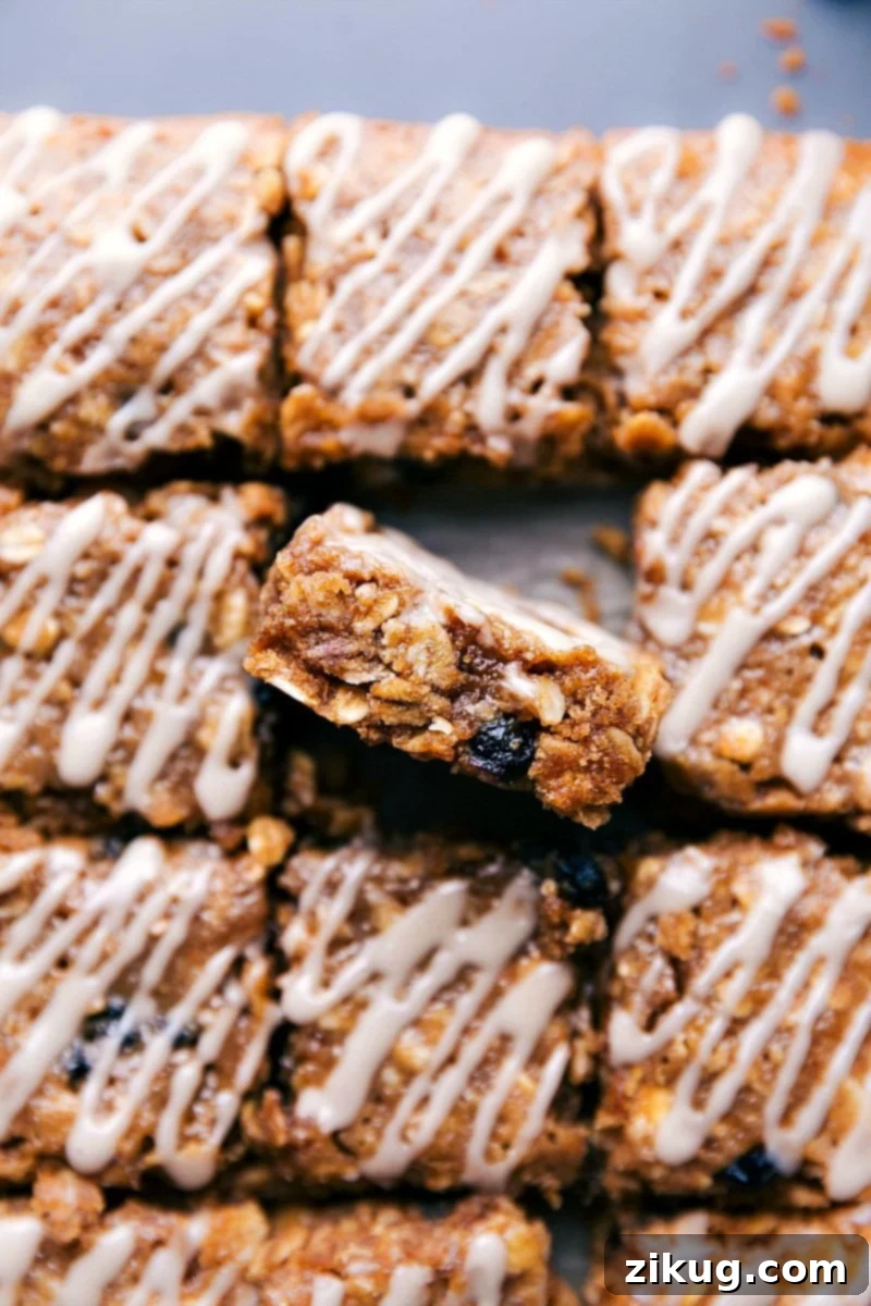 Image of the blueberry oatmeal squares cut in squares with one of them sitting up showing the inside, garnished with fresh blueberries and a drizzle of vanilla glaze.