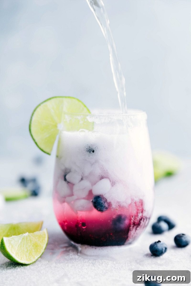 Chilled Limeberry Fizz 5 Multiple glasses of the blueberry mandarin-lime spritzer ready to be served, adorned with sugar rims and fresh fruit, on a wooden surface.